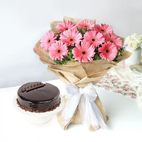 Fresh pink gerberas in rustic jute wrapping with a rich chocolate truffle cake for sweet celebrations. Pink gerbera bouquet with chocolate truffle cake for birthday and anniversary gift